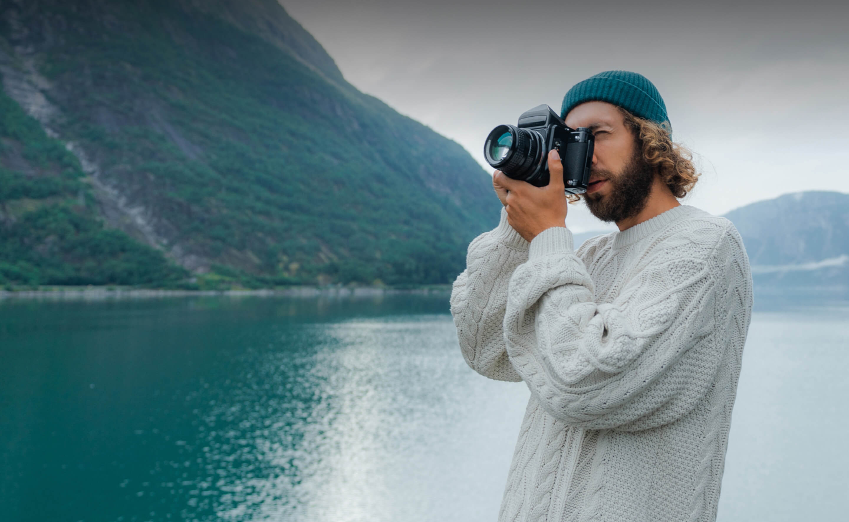 Ein Mann mit Strickpullover fotografiert eine beeindruckende Berg- und Seenlandschaft.