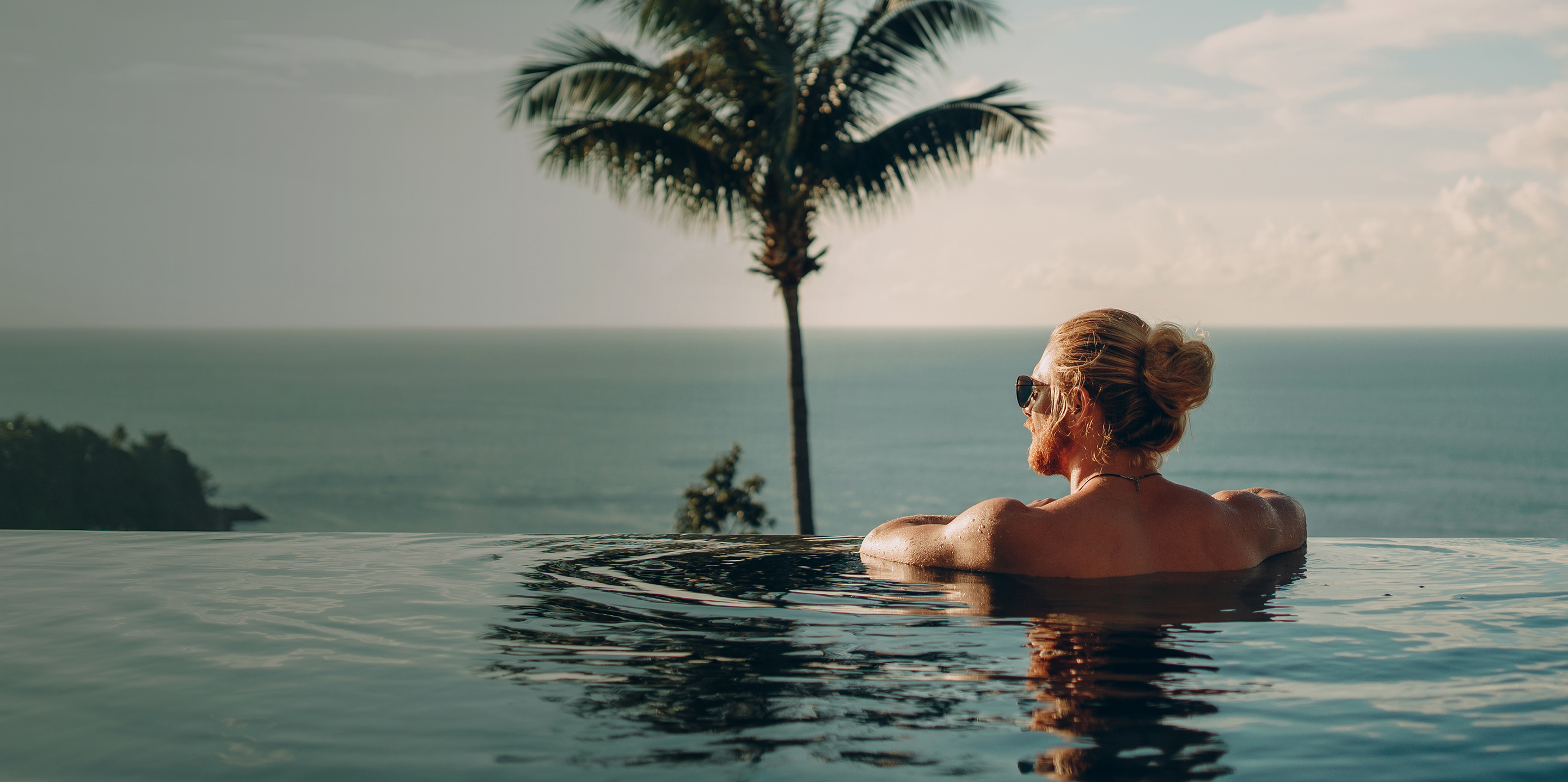 Mann im Infinity-Pool schaut aufs Meer