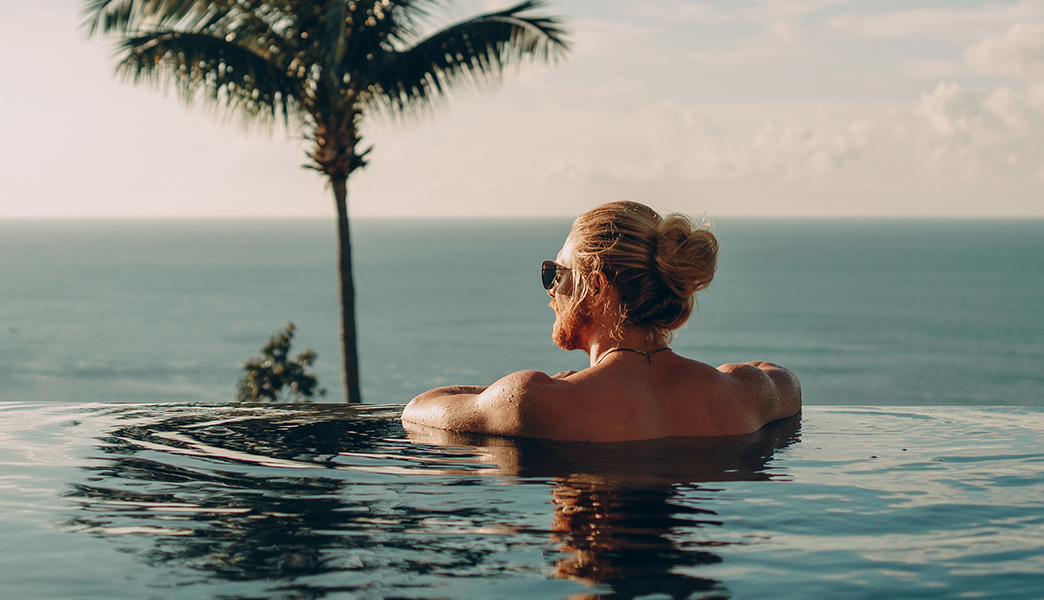 Ein Mann im Infinity-Pool schaut aufs Meer