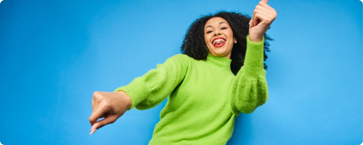 Frau im grünen Pullover tanzt vor blauer Wand