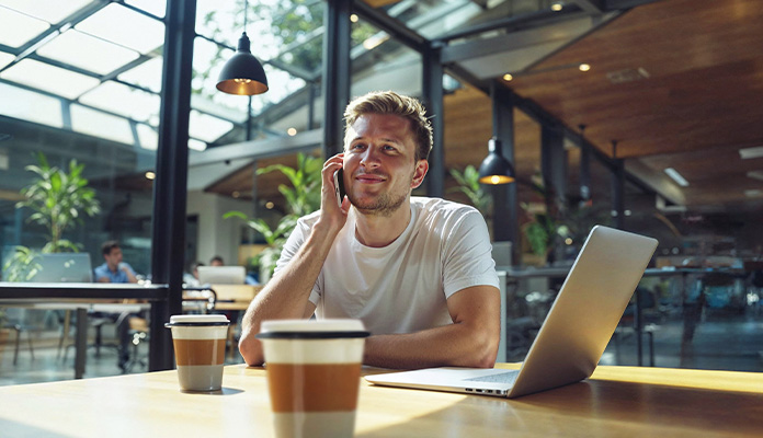 Ein Mann telefoniert mit Kaffee und Laptop vor sich im Büro