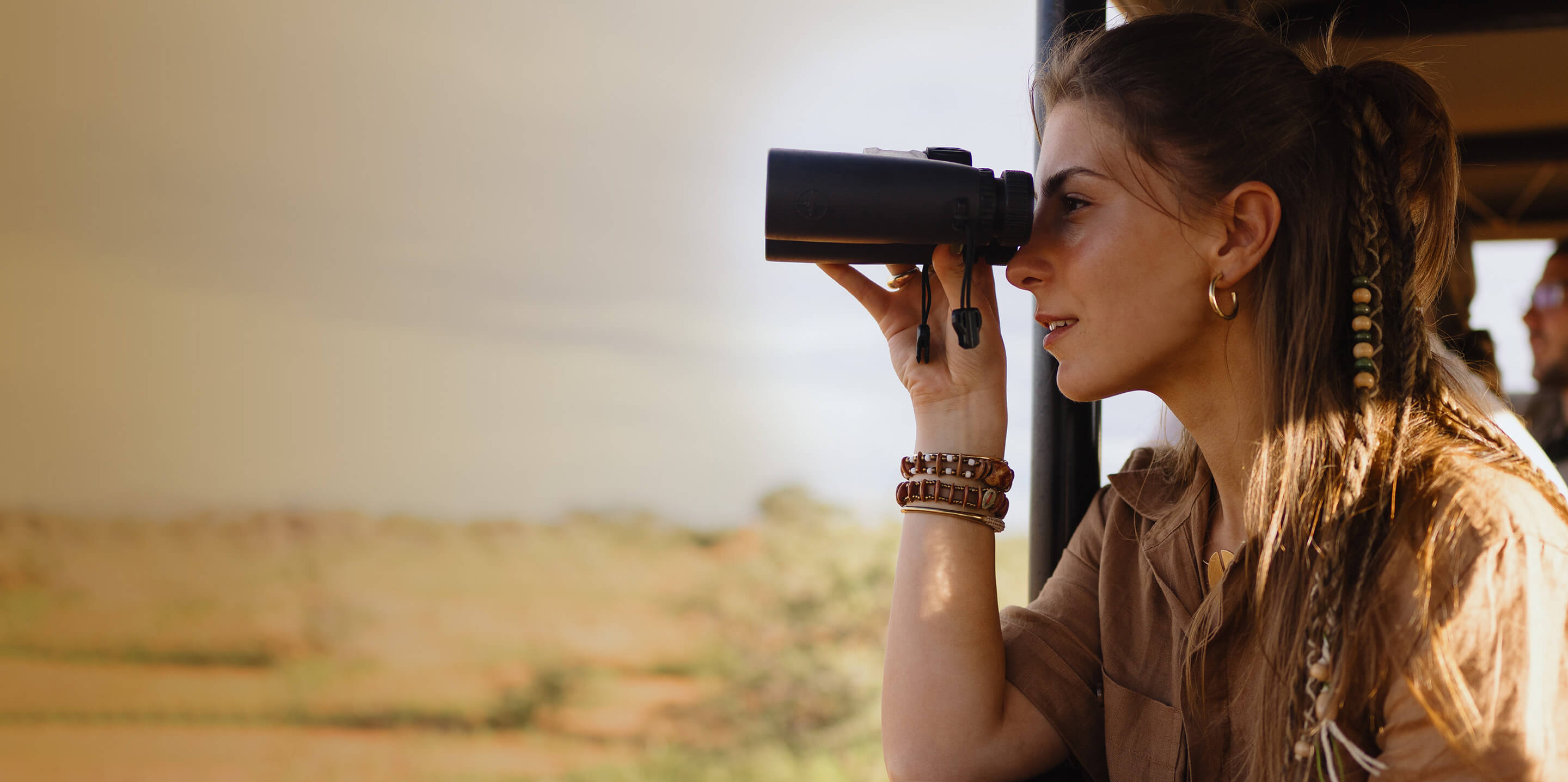 Eine Frau auf Safari schaut mit einem Fernglas aus dem Fahrzeug